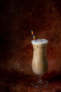 Iced Latte in a hurricane glass with a rainbow striped straw against a brown backdrop