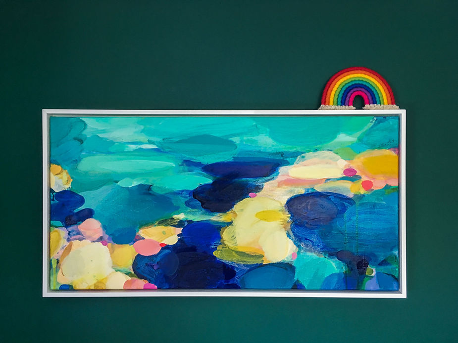 rainbow wrap wall hanging on top of a colourful painting on a dark green wall