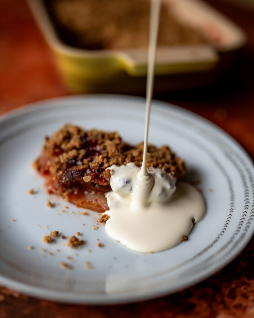 Cream pouring on a slice of crumble on a white plate