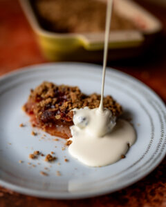 Cream drizzling on a slice of plum crumble on a white plate